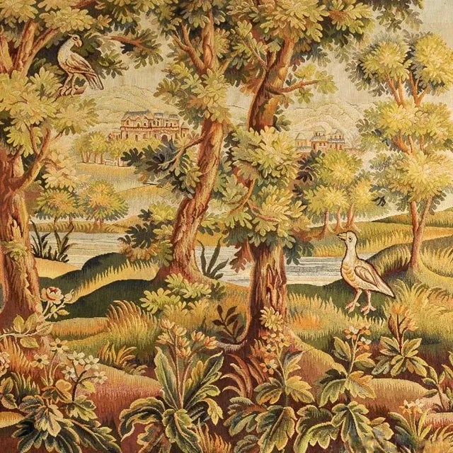 A fine landscape tapestry executed in wool and silk, depicting a leafy view over a river bank through large trees to a...