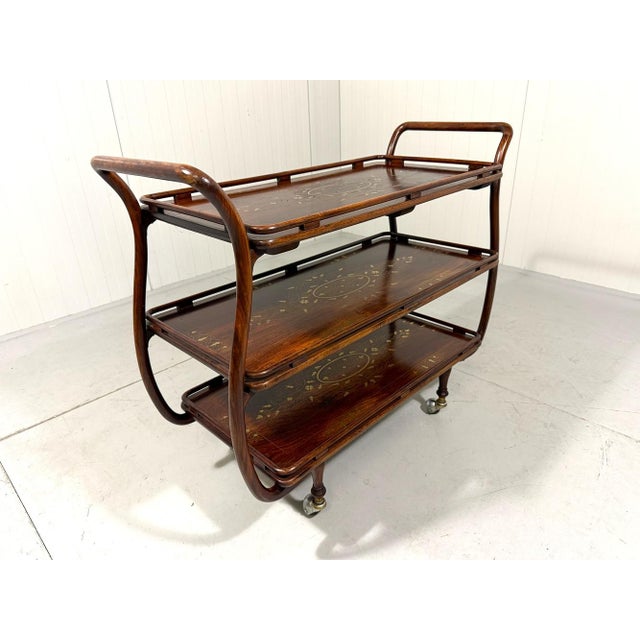 Stylish serving trolley, Italy. Elegant shaped bentwood frame, three anglo indian teak wooden table tops inlaid with a...