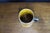 Yellow glazed ceramic tankard featuring a humorous illustrated scene of a man drinking from a tankard, accompanied by a...