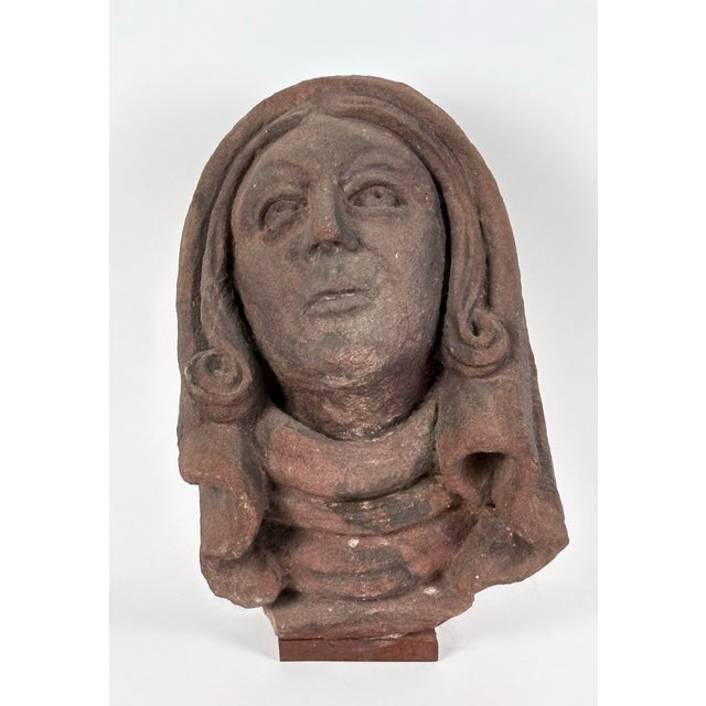 A dramatically carved 15th Century French sandstone head of a female saint. The hooded and cloaked figure looks...