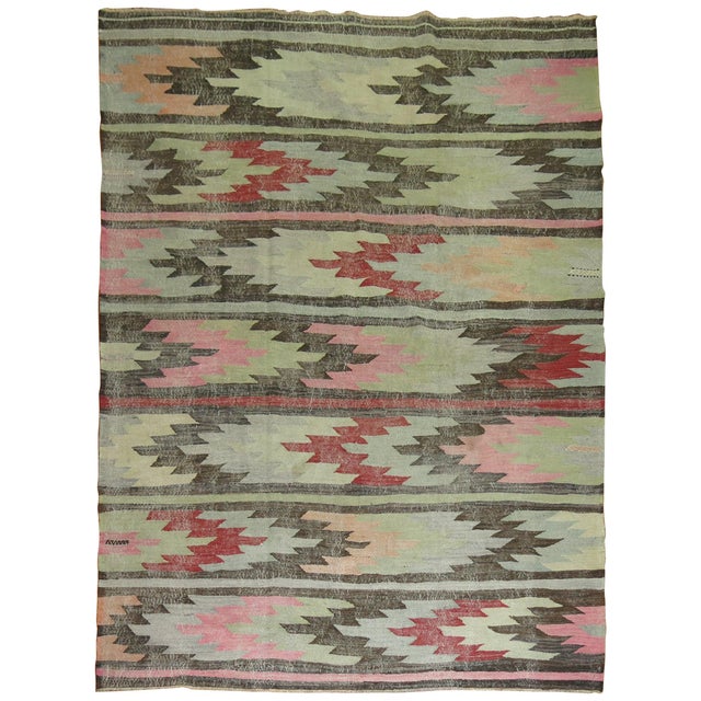 Mid-20th century evenly worn Turkish kilim in pink, green, cream, red, blue and gray accents on a charcoal field....