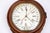 An antique wall clock in a mahogany case with a large round bezel, white dial with black hour and minute hands, bold black...