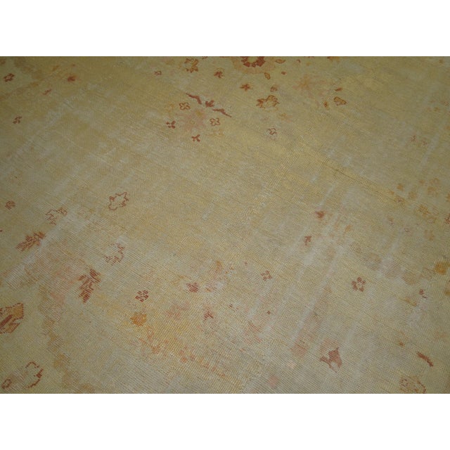 An early 20th century worn oversize antique Turkish Oushak rug in soft colors. Ivory field accents in pink, brick red,...
