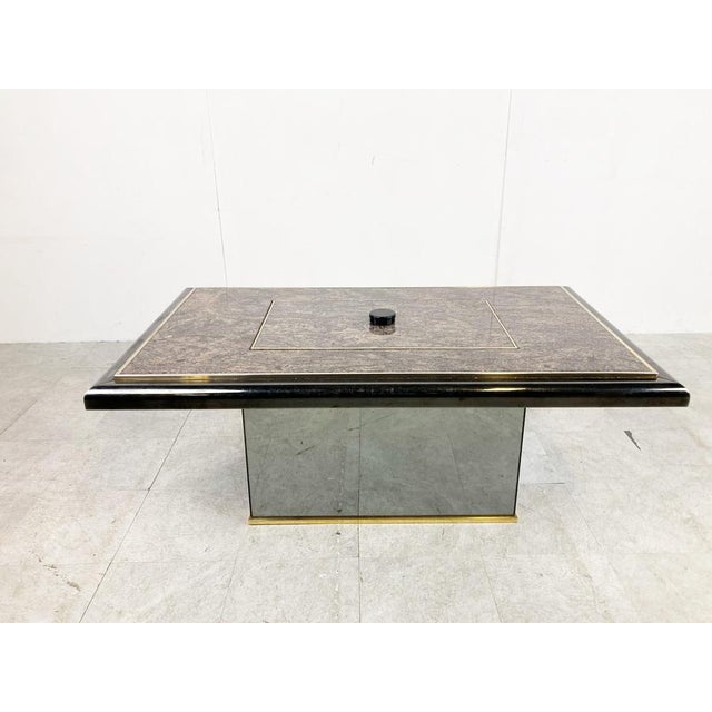 Unique coffee table that, with a twist of the knob, reveals a hidden bar compartment. The coffee has a brass and mirrored...