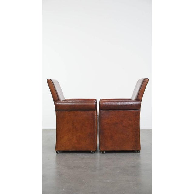 Offered this characterful vintage set of 2 sheep leather dining chairs with black piping on casters. These fun and...