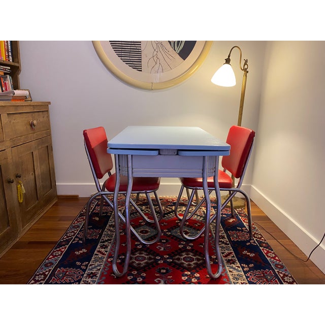 A charming 1940s enamel-top extendable dining table in a soft powder blue, paired with two matching metal chairs with red...