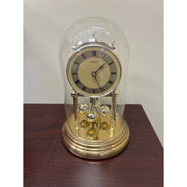 A 9-inch-tall gold quartz anniversary dome clock by Linden with roman numerals and a rotating pendulum mechanism. It's...