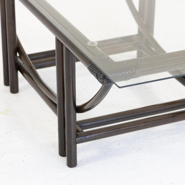 Low coffee table made in the 1970s with a dark-dyed rattan frame and transparent glass top. The base features an elegant...