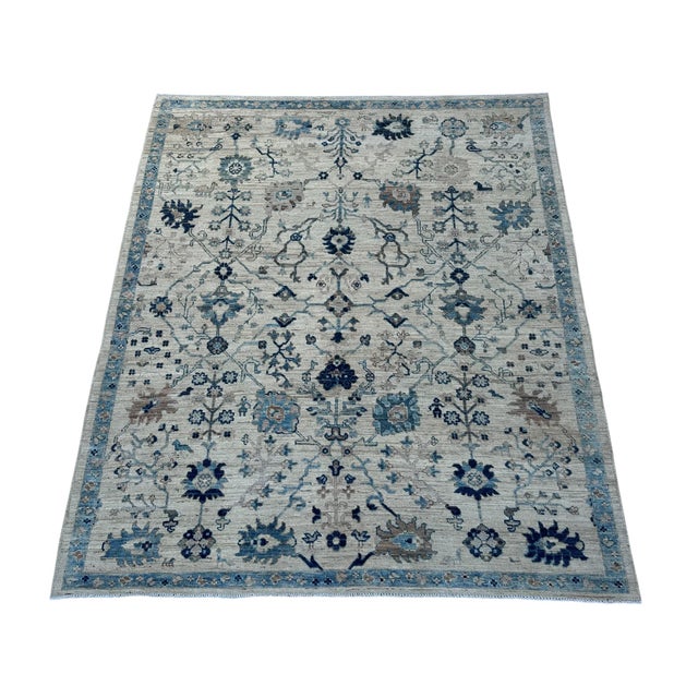 Branching floral stems, rosettes, and small bird motifs form a detailed garden pattern across this handmade Oushak wool...