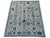 Branching floral stems, rosettes, and small bird motifs form a detailed garden pattern across this handmade Oushak wool...