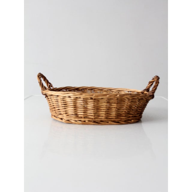 Vintage handwoven wicker gathering basket featuring an oval form, twisted side handles, and warm natural tones. Perfect as...