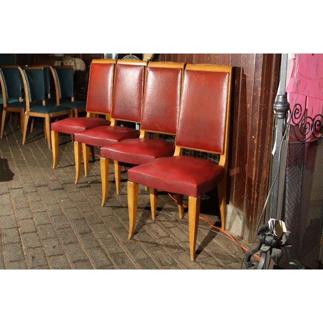 Set of four high back French dining chairs upholstered in red oil cloth with medium wood colored frames. Wood frames are...