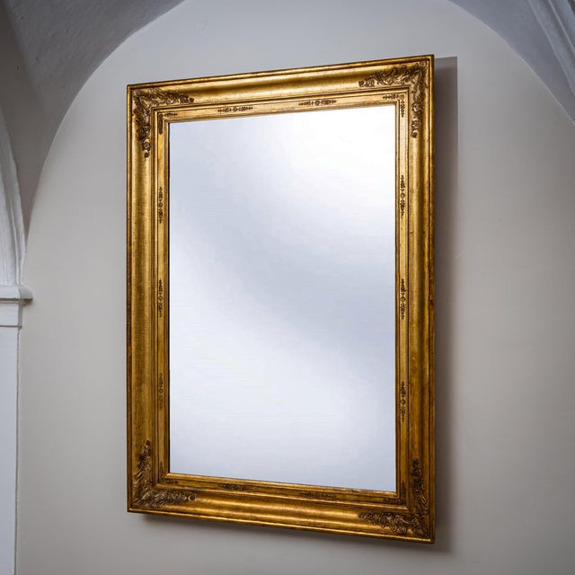Large vertical wall mirror in a gilt and molded Empire frame with applied stucco decoration. The mirror plate is of a...