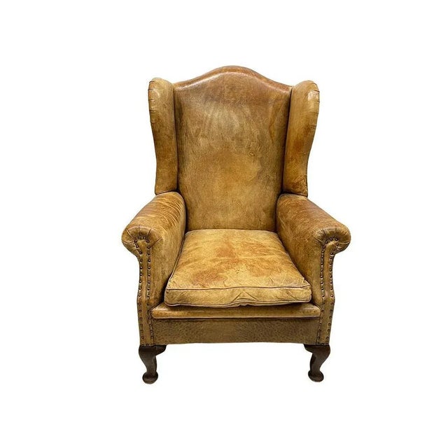 A leather wingback chair A late 19th Century wingback chair in raw leather upholstery with dark oak Queen Anne front legs...