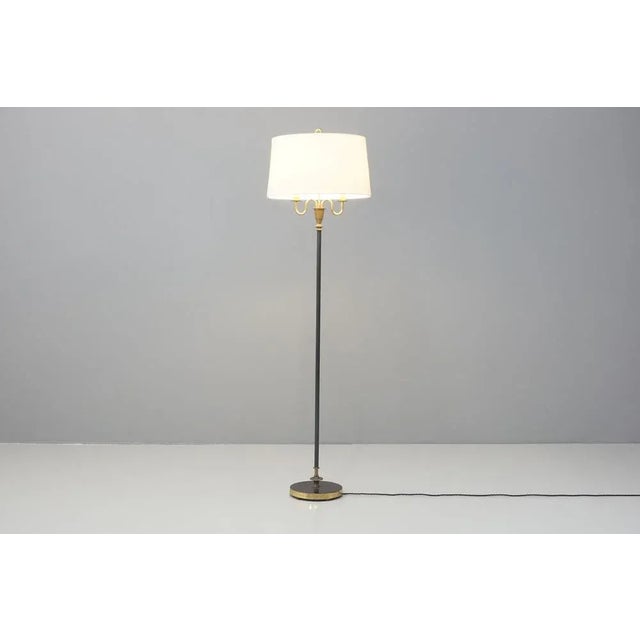 A Mid-Century French floor lamp with a blackened steel shaft and base, with brass details at the base and neck. Double...