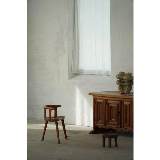 A Scandinavian folk art three-legged chair, carved in solid pine and finished with a warm lacquer, early 20th century. The...