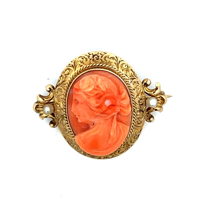 A finely crafted Victorian cameo brooch dating to the late 19th century, centered by a hand-carved Mediterranean coral...