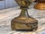 A brass mantel clock in the form of a two-handled urn, with the clock face set into the body of the vase. The handles...