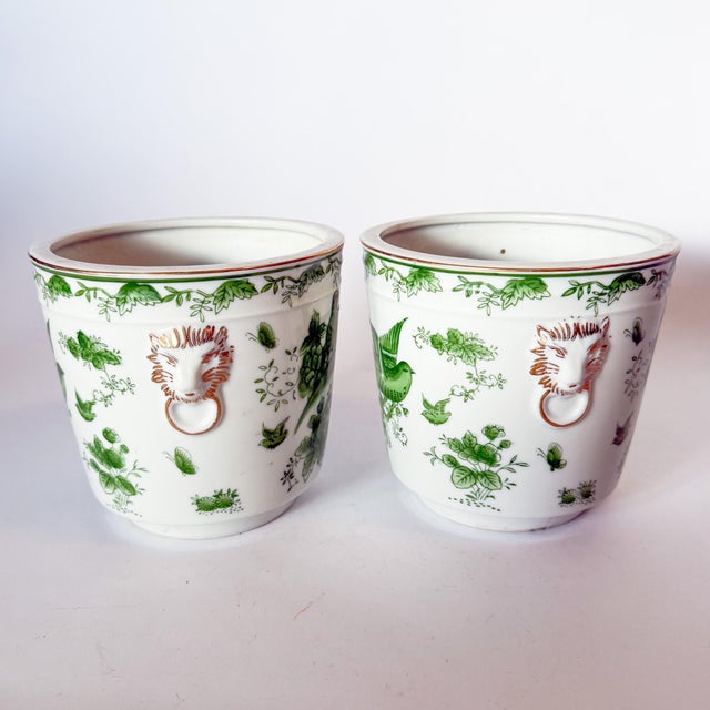Lovely pair of porcelain cache pot planters, mid century, with green bird motifs and gilt lions head handles. They have...