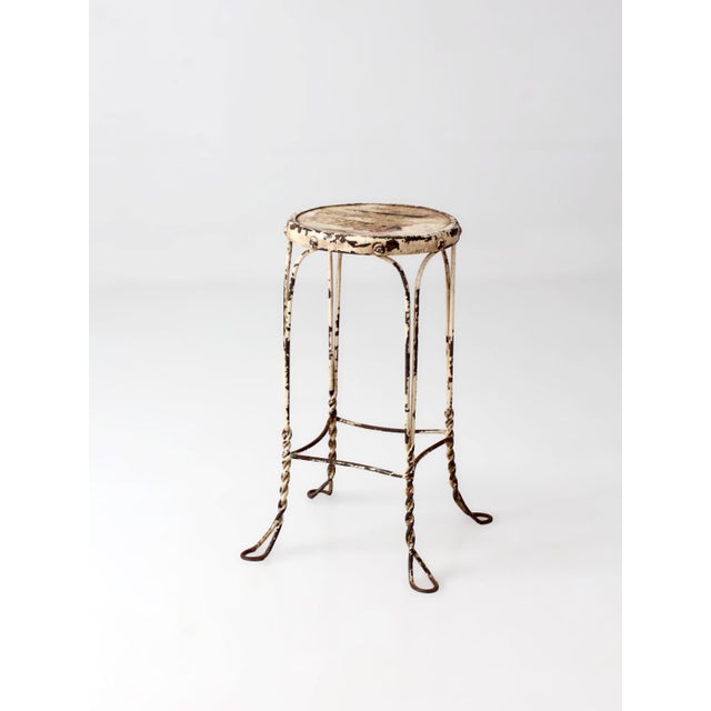 An early 20th century twisted iron garden stool or plant stand featuring looping feet and a weathered wood veneer inset...