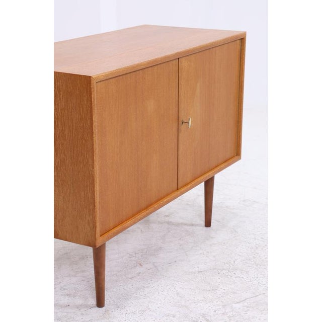 Vintage teak chest of drawers with a clean front, two doors and a spacious interior compartment. The slender tapered legs...