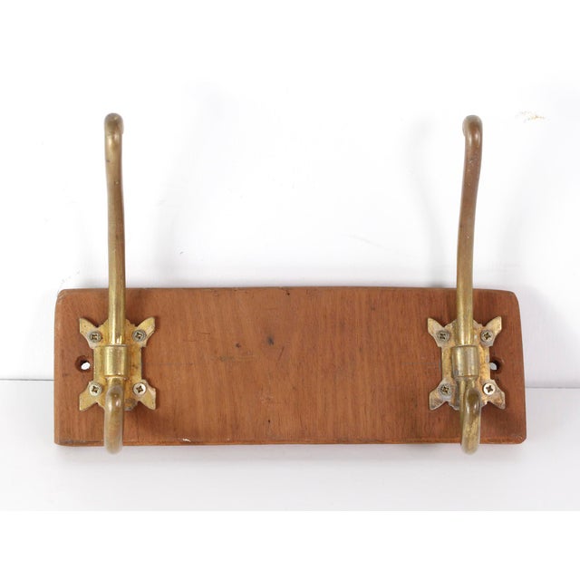 European imported large double brass hooks on a medium tone wood plank. The manufacturer and exact date of creation are...