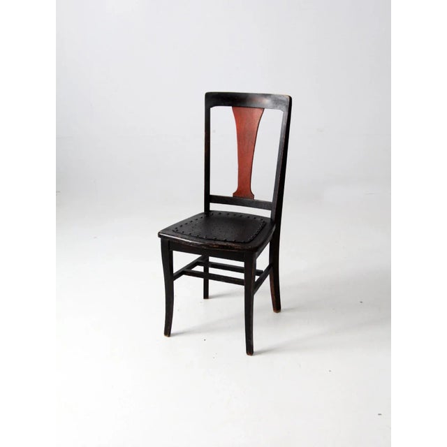 An early 20th-century Arts and Crafts-style side chair featuring a distinctive black fiddle back with a contrasting red...