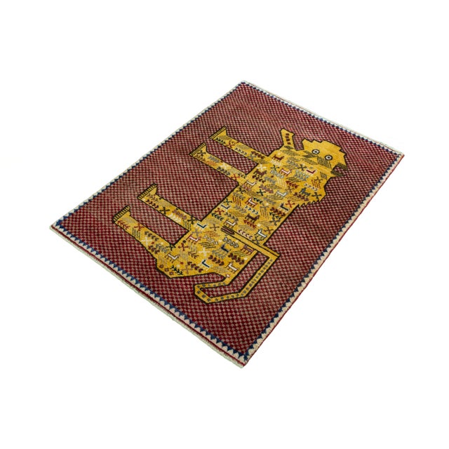 This hand-knotted Gabbeh nomad rug features a unique, colorful animal motif on a bold red checkerboard-like background....