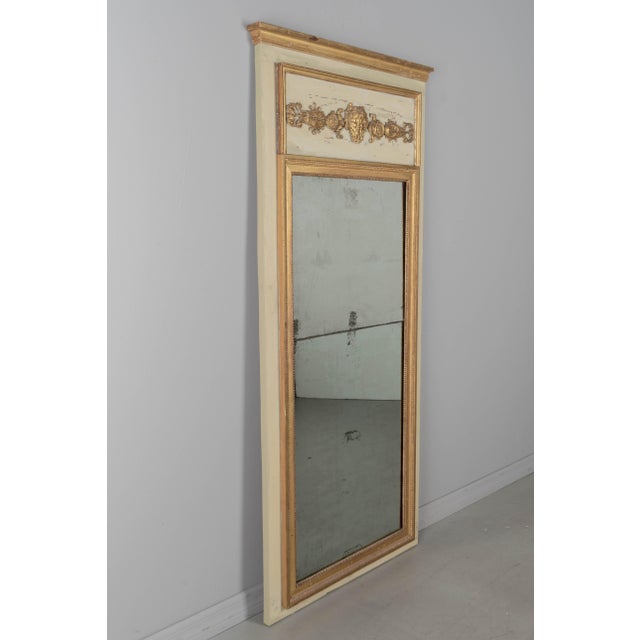 An early 20th century French Louis XVI style trumeau mirror with painted pine frame and gilded trim. Carved giltwood...