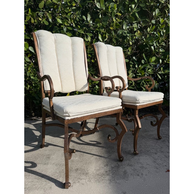 A matched pair of vintage hammered iron lounge chairs featuring sculptural scroll arms, decorative brass finials, and a...