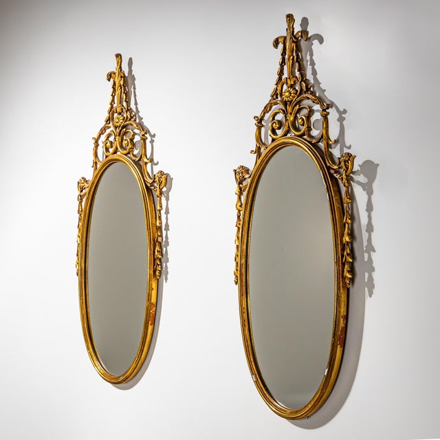 Pair of gilt wood and stucco mirrors featuring oval frames and elaborate crestings. The crest elements are richly...