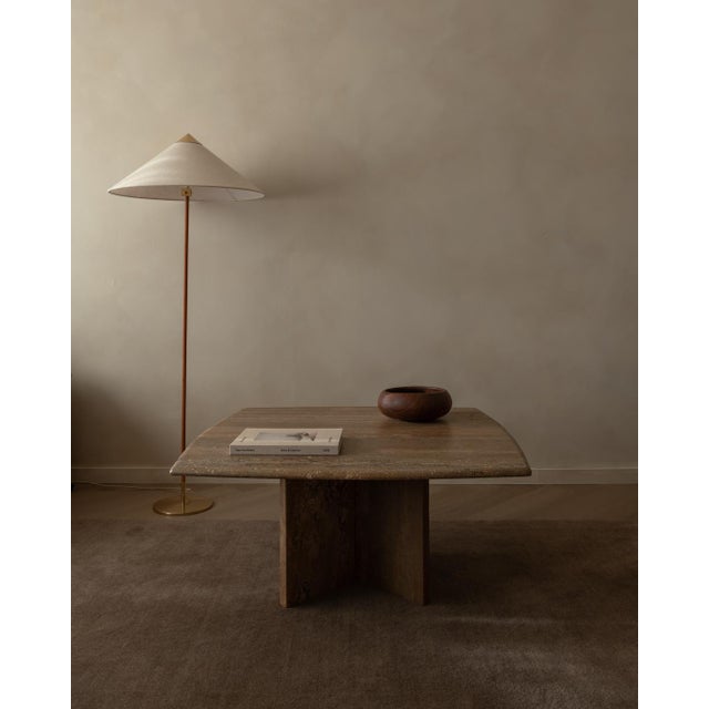 This sculptural coffee table is carved from solid brown travertine and stands on two separate L-shaped legs, creating a...