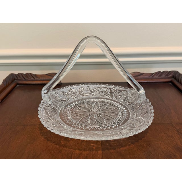 Elegant vintage pressed glass handled basket featuring intricate floral and scroll motifs, a starburst medallion center,...