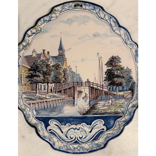 Antique hand painted Delft wall plaque with scalloped blue edge depicting a Dutch canal scene. Circa late 19th or early...
