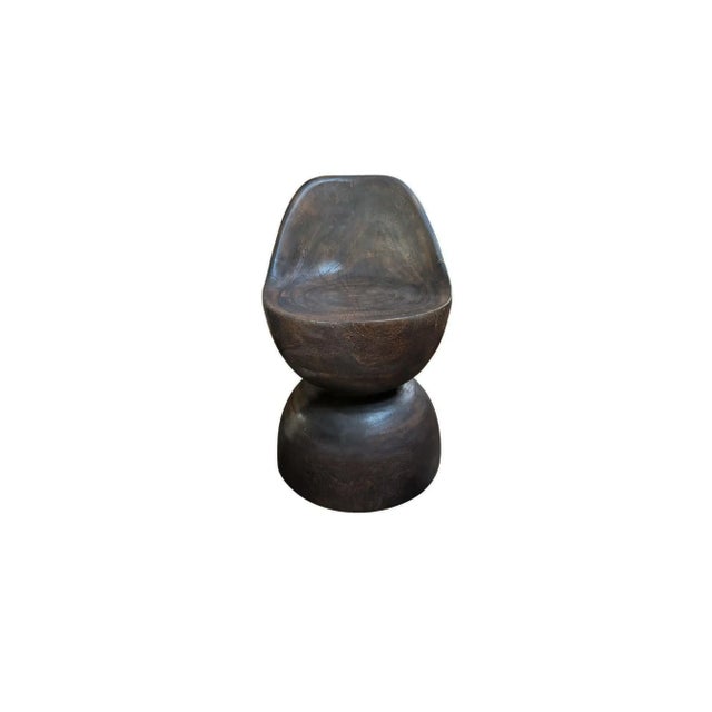 Elevate your space with this sculptural Suar wood chair, expertly carved from a single, solid block of timber. Its fluid,...