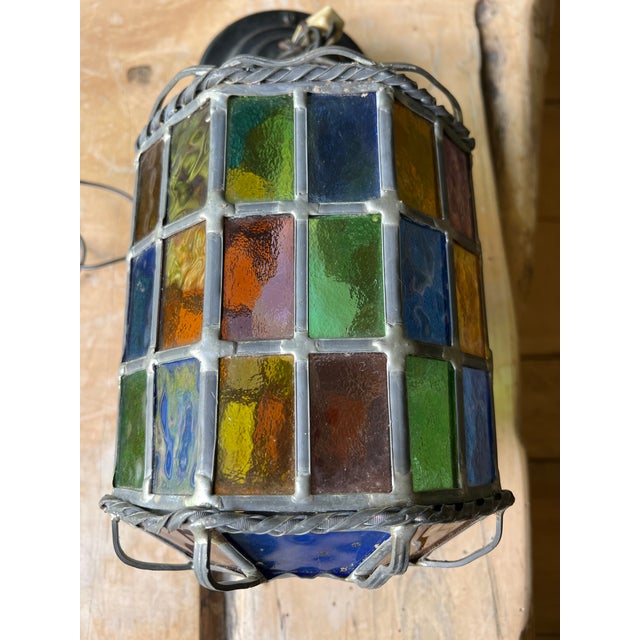 This vintage stained glass pendant lamp features a multicolor paneled design held together by twisted metal trim.