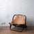 A sculptural mid-century lounge chair in rattan with a dark bent-frame structure and a tan leather sling seat and back....