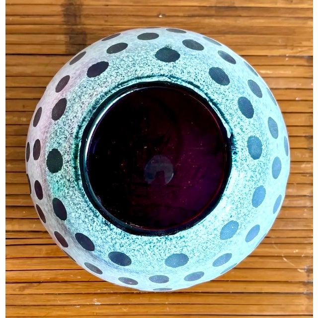 A bold and graphic hand-blown art glass vase featuring a frosted white surface layered over deep amethyst glass, carved...