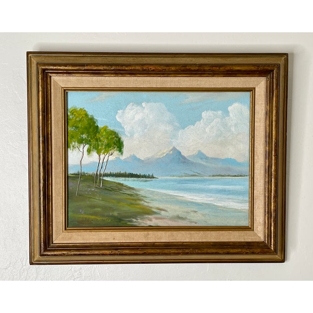 A deserted beachscape with jagged mountain peaks in the distance. Voluminous clouds behind the mountains add a dreamlike...