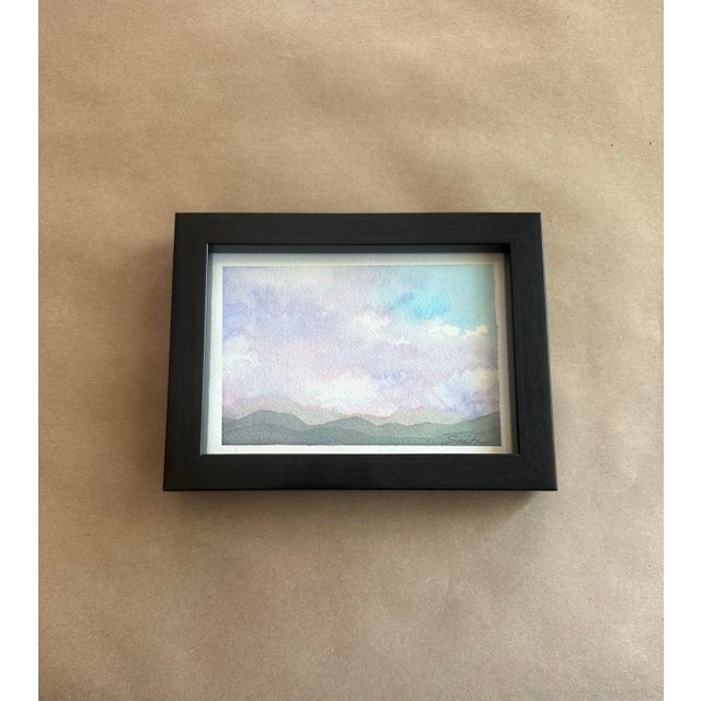 A serene miniature landscape rendered in delicate watercolor washes of lavender, mist blue, and soft green. Gentle rolling...