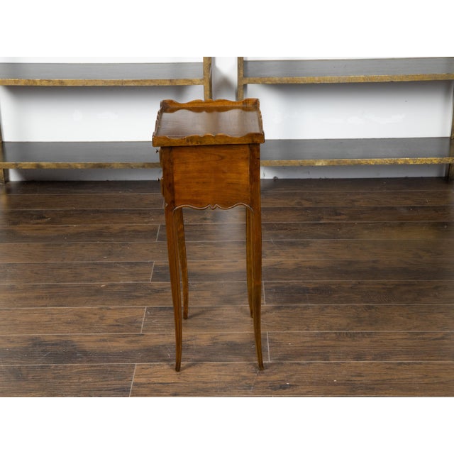 A French walnut side table from the early 20th century, with carved tray top and four small drawers. Created in France...
