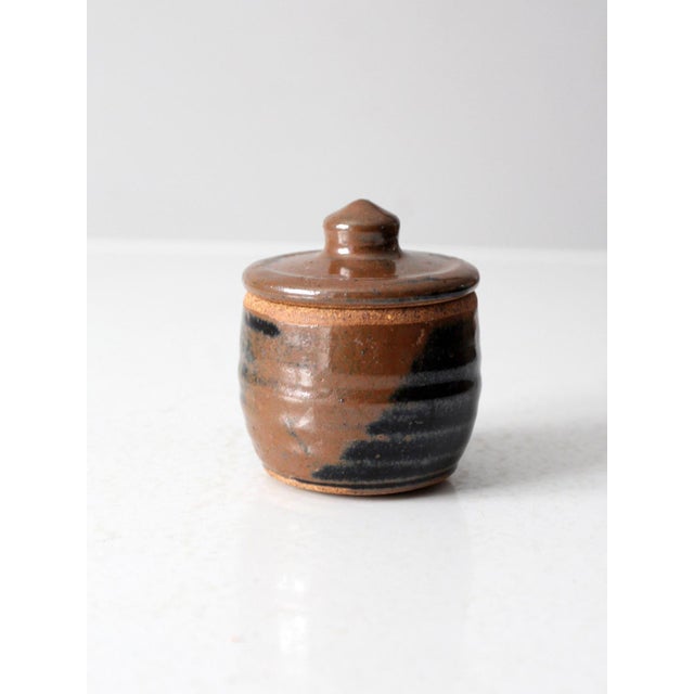 This vintage studio pottery jar is signed by the artist and features a ribbed design with a rich brown glaze and bold...