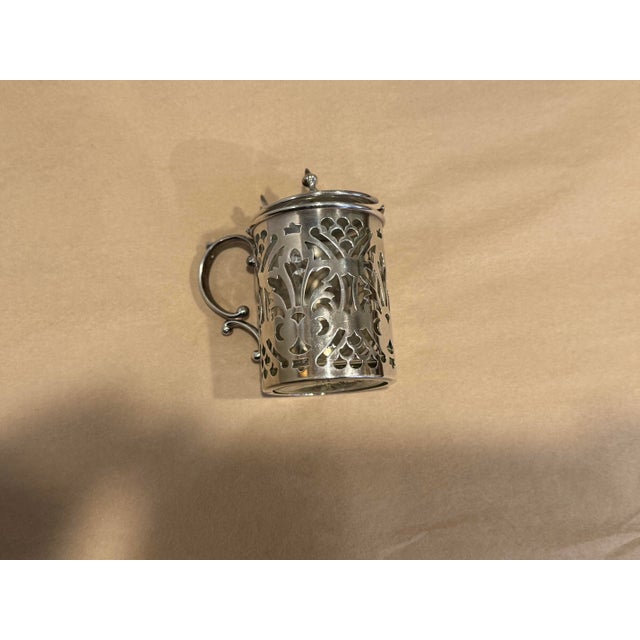 This is an antique sterling silver mustard pot. It has a cylindrical shape with a hinged lid. It has intricate open work...