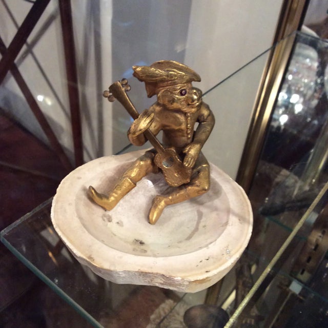 Bronze monkey playing an instrument sitting on the rim of a slice of stone. The eyes have stones set in them.