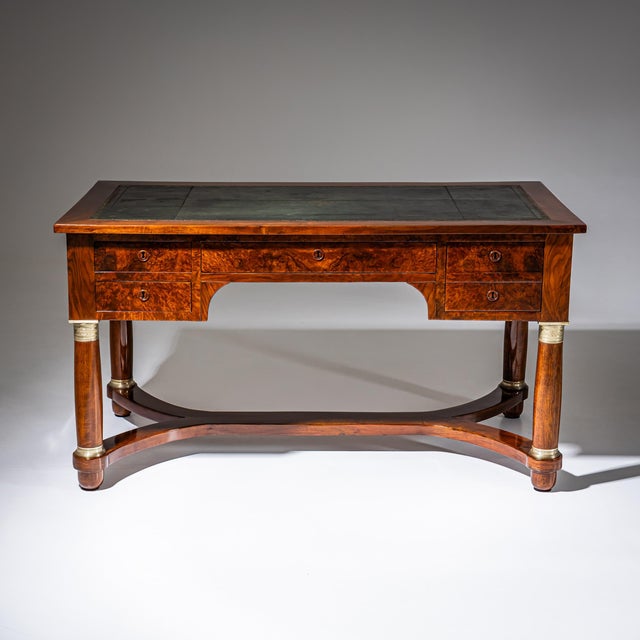 Large desk veneered in walnut and burl wood, raised on four tapered legs with brass bases and capitals, connected by an...