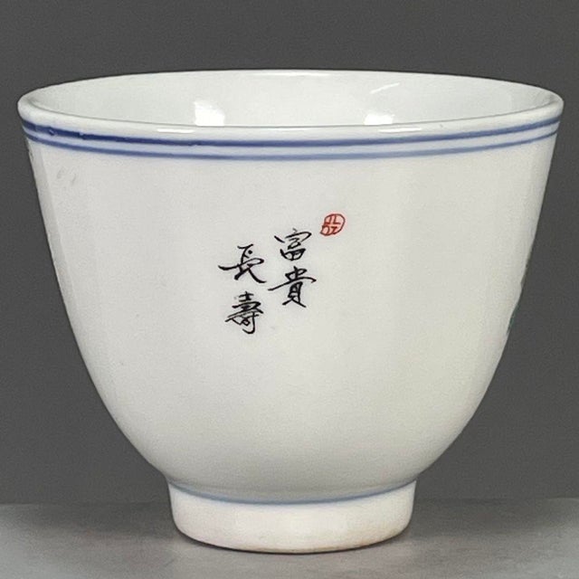 A charming Chinese porcelain tea cup. The exterior is finely hand-painted in vibrant Famille Rose enamels, featuring two...