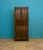 A 1920s oak kitchen larder cupboard in the Tudor Revival style, featuring vented upper doors, a central fall-front...