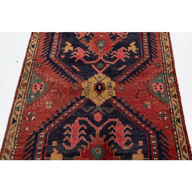 This hand-knotted wool rug has a navy blue and red field with multicolor accents all over the design. This rug measures...