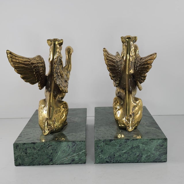 These brass griffin bookends, with elegant wings and fierce expressions, rest on green marble bases. They provide...