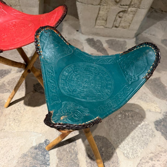 For your consideration, a pair of vintage Mexican hand-tooled leather tripod folding stools. One red and one green....